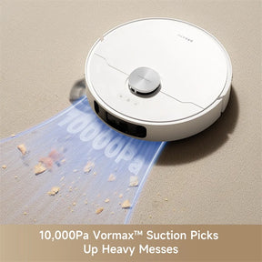White robotic vacuum on carpet, top sensor disc and edge brushes visible.